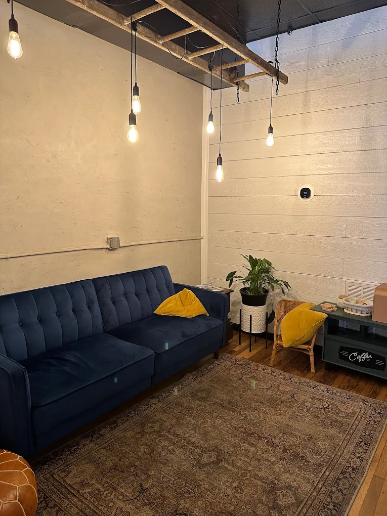 The back lounge: a navy velvet sofa with yellow pillows on a vintage rug, under Edison bulbs hung from an old ladder.