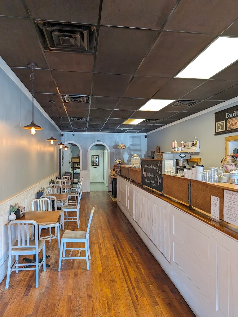 The long main room: wood floors, metal chairs at wood tables, pendant lights, and the counter running along the right.